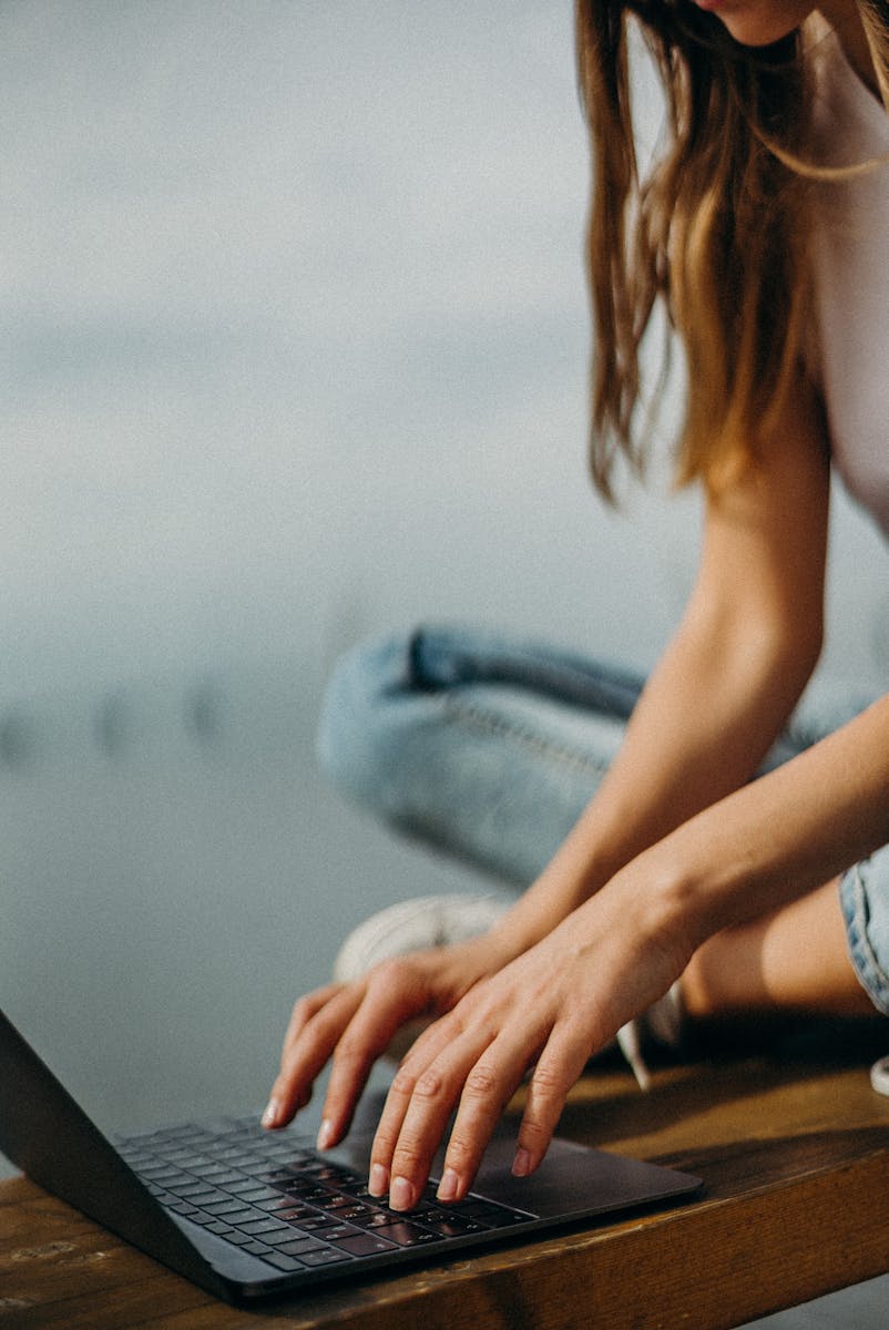 Una giovane donna che lavora a distanza sul suo computer portatile in riva al mare.